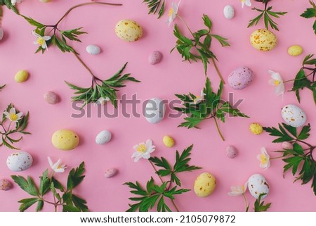 Happy Easter!  Colorful Easter chocolate eggs and spring flowers flat lay on pink background. Stylish easter layout. Greeting card or banner. Candy and flowers composition