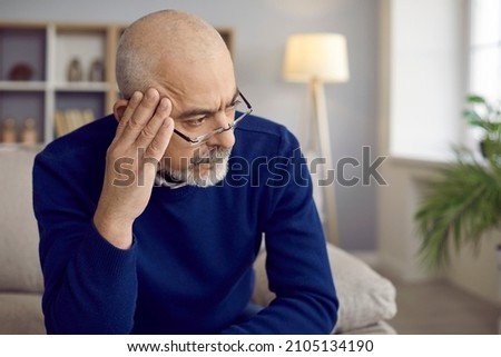Older man with serious and thoughtful expression looks away thinking about something important. Close up head shot of man with glasses holding hand near his head. Old age, problem and people concept. Royalty-Free Stock Photo #2105134190