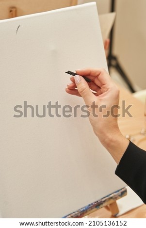 a woman's hand with a black crayon is raised to a white blank canvas