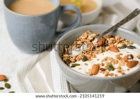 Concept of breakfast with granola muesli, yogurt, pumpkin seeds, almonds and coconut pieces in boul with a spoon on the light table. Selective focus, low depth of field Royalty-Free Stock Photo #2105141219