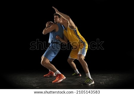 Interception of the ball. Two male athletes, competing basketball players in motion isolated over black background. Concept of professional sport, lifestyle, action and motion