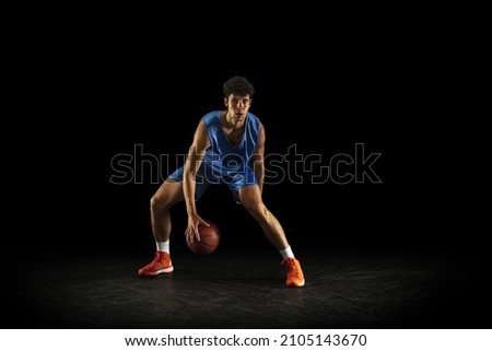 Dribbling. Front view. Young Caucasian professional basketballer training with ball isolated on black background. Concept of active life, motion, energy, sport.