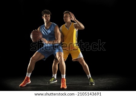 Defending. Two male athletes, competing basketball players in motion isolated over black background. Concept of professional sport, lifestyle, action and motion