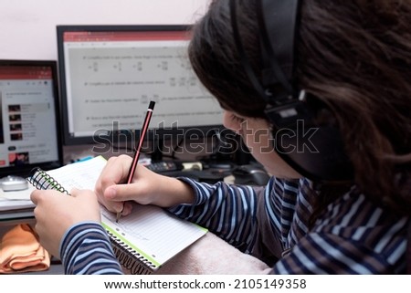 Transgender teenager studying in front of the computer unfocused, at his messy desk, listening to music videos and drawing in his notebook instead of doing homework.