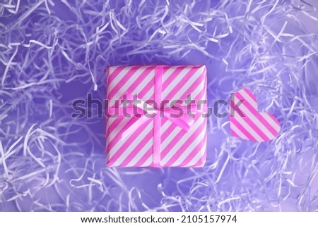 Gift with pink ribbon ribbon on a background with a Very Peri color paper filler. The tradition of giving gifts to loved ones on Valentine's Day, holidays, birthdays. Pink and white pinstripe Royalty-Free Stock Photo #2105157974