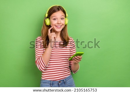 Photo of cheerful blogger lady hold phone listen song wear headphones striped shirt isolated green color background