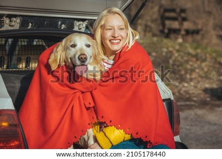 A beautiful woman hugs her Golden Retriever dog and covers her with a red blanket from the cold. Autumn picnic walk with your pet in the countryside. Woman and cute dog enjoying outdoors