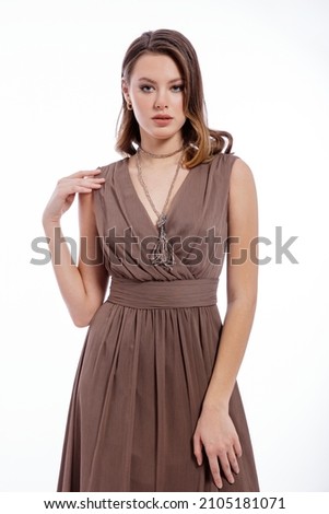 High fashion photo of beautiful elegant young woman in a pretty beige brown dress with a neckline, necklace posing on white background. Slim figure, make up,  luxurious hair, shiny curls. Studio Shot