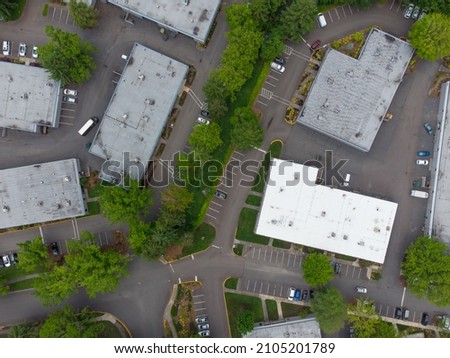 Aerial view. Small suburb. Industrial Zone. Roofs of large one-story rooms. Garages. Warehouses. Lots of greenery. Paved roads. Cars. There are no people in the photo.