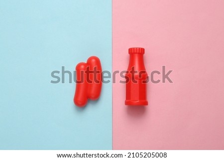 Toy plastic sausage with ketchup on a blue-pink pastel background. Top view