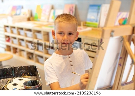  Smiling blond boy draws on canvas in the workshop. Drawing lessons for children