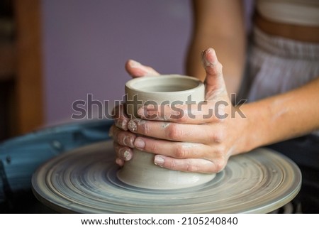 Close-up of a woman's hands shaping a ceramic pot on the lathe