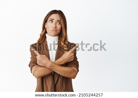 Portrait of indecisive woman pointing sideways with confused face, having doubts while making her choice, white background