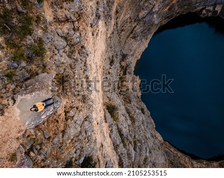 Drone shot of tourist sitting on rock right next to the Red lake in April at Imotski, Dalmatia, Croatia