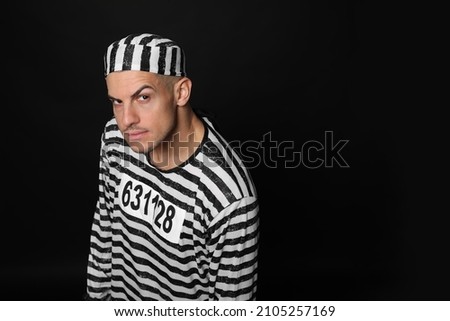 Prisoner in striped uniform on black background, space for text Royalty-Free Stock Photo #2105257169