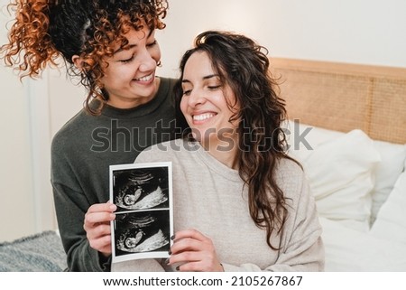 LGBT lesbian couple holding ultrasound photo scan of growing baby in pregnancy time - Focus on right woman face Royalty-Free Stock Photo #2105267867