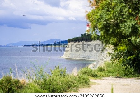 High rocky coast of the Black Sea. A lighthouse on the edge of a cliff and a plane taking off against the background of a lighthouse. Blue sea summer, white clouds.