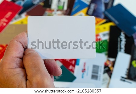 Blank plastic card in hand on blurred background of various plastic loyalty cards