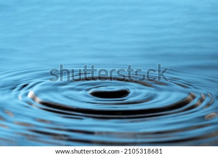 On the surface of the blue water, wavy circles spread in different directions. Place for advertisement and text Royalty-Free Stock Photo #2105318681
