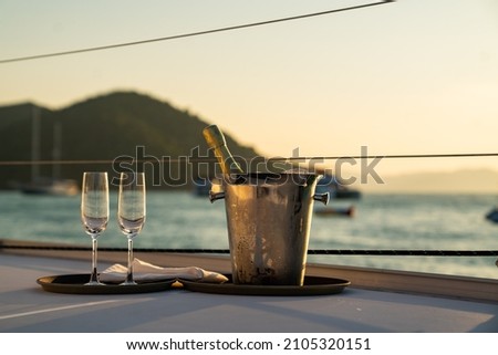 Champagne bottle in ice bucket with champagne glass for serving to passenger tourist on luxury catamaran boat sailing in the ocean at summer sunset. Tropical travel vacation sail yacht trip concept Royalty-Free Stock Photo #2105320151