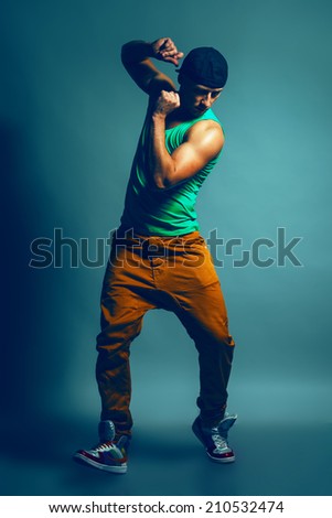 Young handsome male hip-hop dancer in trendy clothing showing some moves over blue background. Studio shot. Copy-space