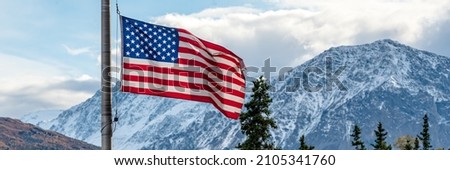 Panoramic mountain setting behind an American, United States flag. Stars and stripes in Alaska. 