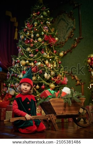 Christmas tales. Cute little girl sits by a wooden cart with gifts and smiles. Vintage room with a fabulous Christmas atmosphere and decoration.