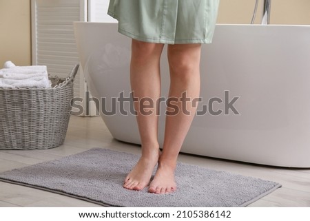 Woman standing on soft grey bath mat near tub at home, closeup Royalty-Free Stock Photo #2105386142