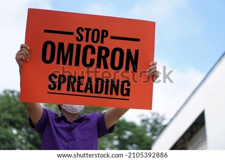 Paper sign with text " Stop Omicron Spreading" held by a man stands outdoor. Concept : Protest, awareness in Omicron Covid-19 or coronavirus spreading around the word that made people panic and detest