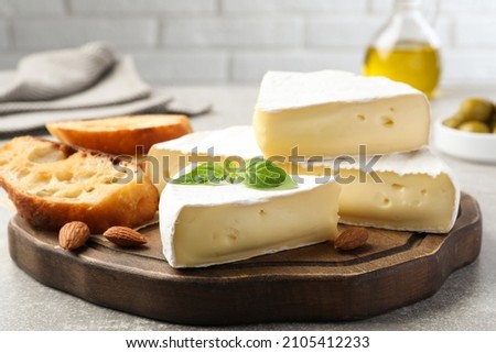 Tasty brie cheese with basil, bread and almonds on wooden board Royalty-Free Stock Photo #2105412233