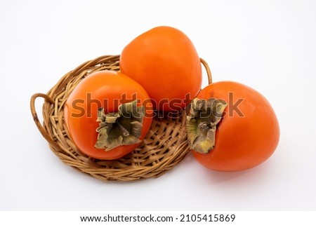 Ripe orange persimmon fruits in wicker basket. Isolated on white background. Royalty-Free Stock Photo #2105415869