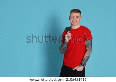 Smiling young man with tattoos on light blue background. Space for text