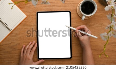 Top view, close-up shot of a female's hand drawing on digital tablet computer over wooden table.