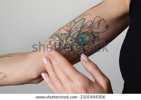 Woman applying cream on her arm with tattoos against light background, closeup Royalty-Free Stock Photo #2105444306
