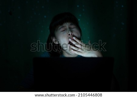 A young woman working with a laptop at night is tired, weary and sleepy. Office syndrome concept Royalty-Free Stock Photo #2105446808