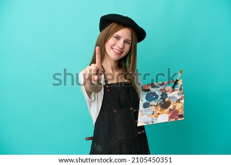 Young artist English woman holding a palette isolated on blue background showing and lifting a finger