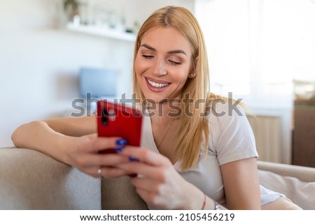 Young woman sit relax on sofa in living room browsing surfing wireless internet on smartphone, millennial girl rest on couch at home message text on modern cellphone, shopping online via website