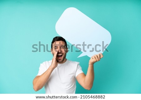 Young handsome caucasian man isolated on blue background holding an empty speech bubble and shouting
