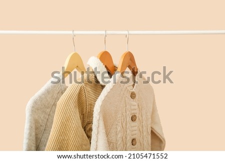 Stylish baby clothes hanging on rack against color background Royalty-Free Stock Photo #2105471552