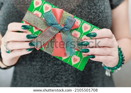 Female hands with long nails and green manicure hold a gift box for the holiday.
