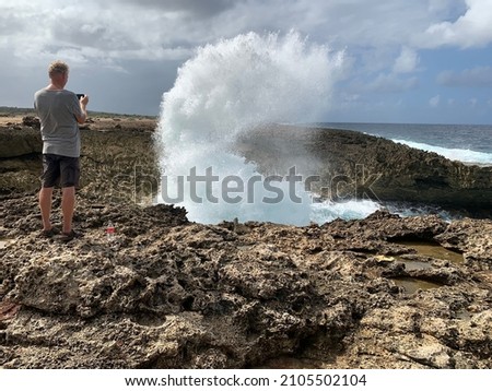 holiday tourist watch the wind-driven waves crash against the jagged coral shore and shatter into a high, splashing fan