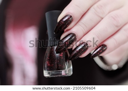 Female hands with long nails and black and red manicure holding a bottle of nail polish