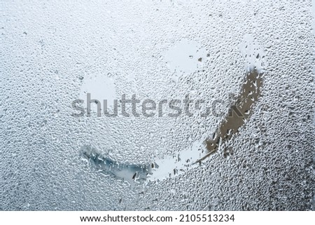 happy smile, hand drawn smiling face icon shape on steamed glass surface or window with rain drops in rainy day. background of raindrops on windowpane with selective focus and noise effects