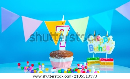 Happy birthday to a seven year old, 7 years old card on a blue background. Cupcake with burning candle, festive background.