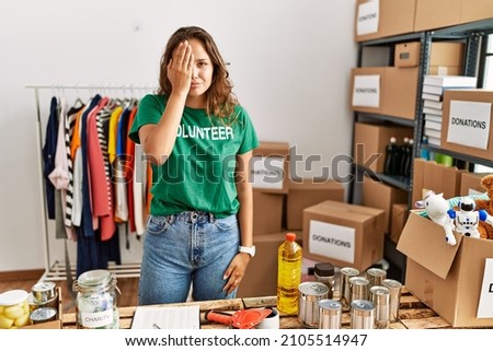 Beautiful hispanic woman wearing volunteer t shirt at donations stand yawning tired covering half face, eye and mouth with hand. face hurts in pain. 
