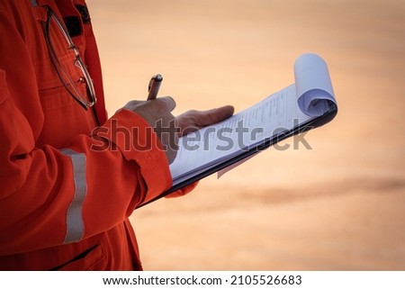 Safety officer or Supervisor is writing note on the checklist paper during perform audit and inspection in oil field operation. Close-up action and selective focus photo.