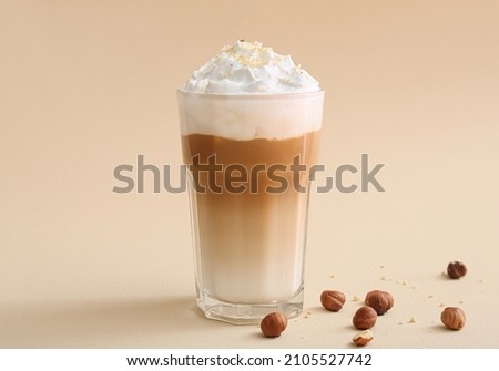 Glass of tasty latte with nuts on beige background Royalty-Free Stock Photo #2105527742
