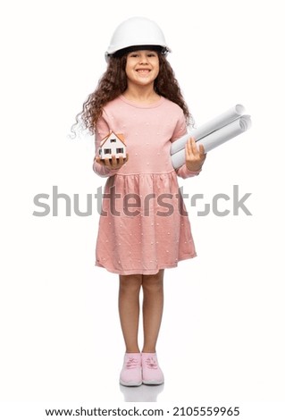 building, real estate and profession concept - smiling little girl in construction helmet holding blueprint and toy house model over white background