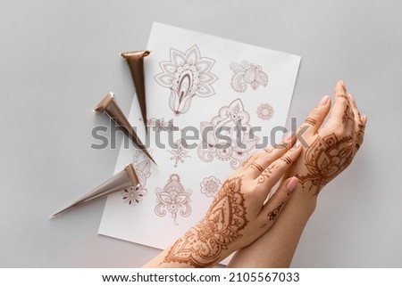 Beautiful female hands with henna tattoo and ornament examples on grey background Royalty-Free Stock Photo #2105567033