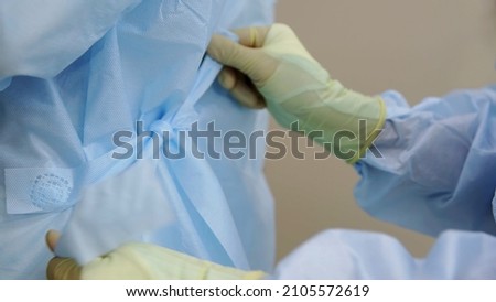 Close-up of professional doctors in uniform, wearing dressing gowns with ties at the back, preparing for surgery. Medicine